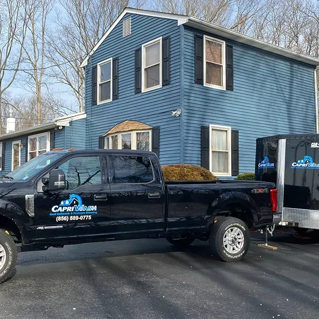 Capri Wash truck and equipment trailer parked outside a blue two-story home at a house washing job